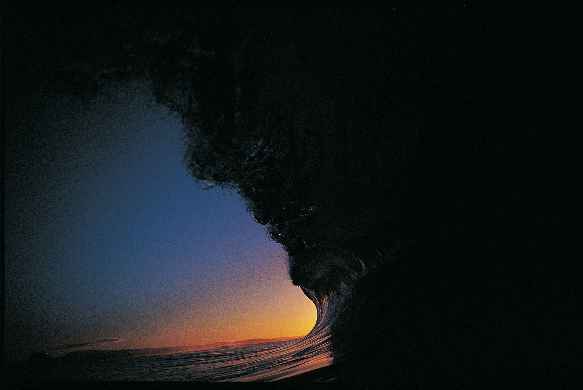 fiery sunset viewed from within an enormous dark wave resembling a man's face